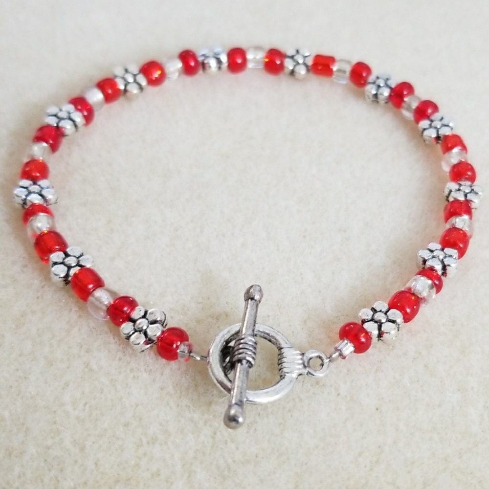 Cute red bracelet featuring silver toned flowers